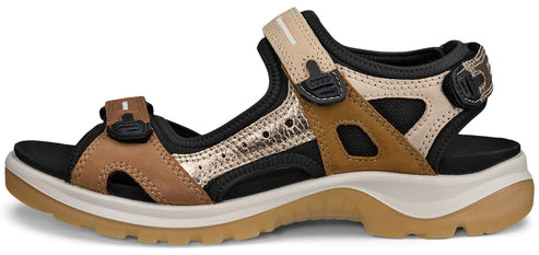A sandal with tan, black, and gold straps and a thick sole.