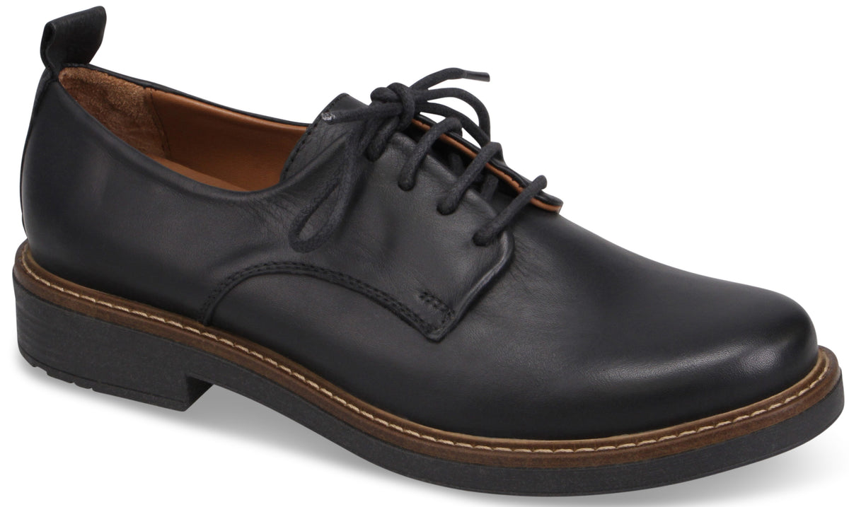 A black leather derby shoe with a rounded toe, five-eyelet lace-up closure, a pull tab at the heel, a light brown welt with contrast stitching, and a low, dark rubber sole.