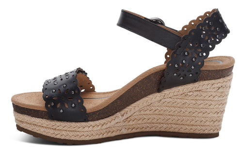 Black wedge heel sandal with cut-out floral pattern and ankle strap.