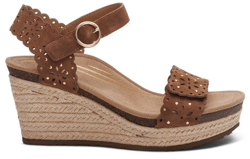 A women's wedge sandal with a light-brown woven wedge heel. The upper straps are brown with a decorative cut-out pattern. An ankle strap with a gold buckle closure is also visible.