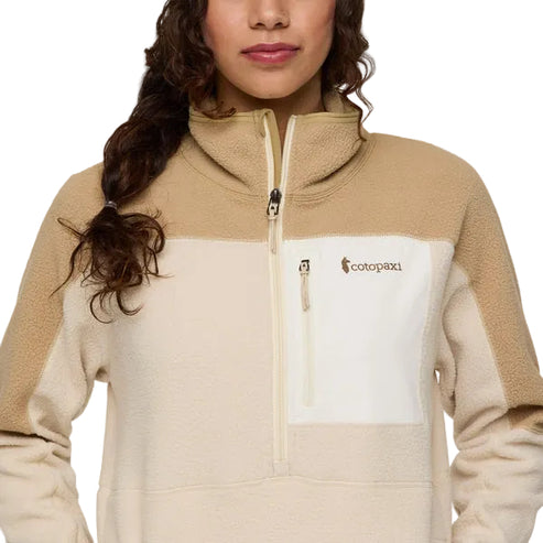 A woman wearing a cream and beige fleece pullover with a quarter zipper and a white pocket featuring a logo.