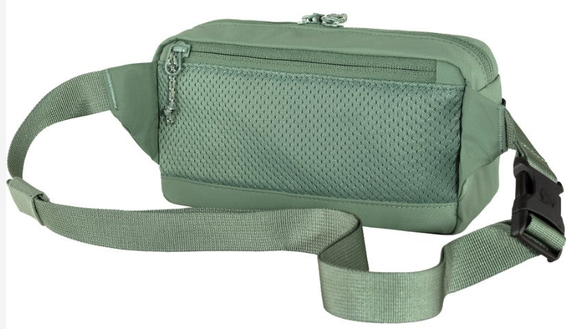 A sage green belt bag with a mesh-covered front zippered pocket, an adjustable strap, and a black side-release buckle.