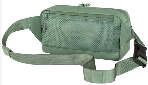A sage green belt bag with a mesh-covered front zippered pocket, an adjustable strap, and a black side-release buckle.