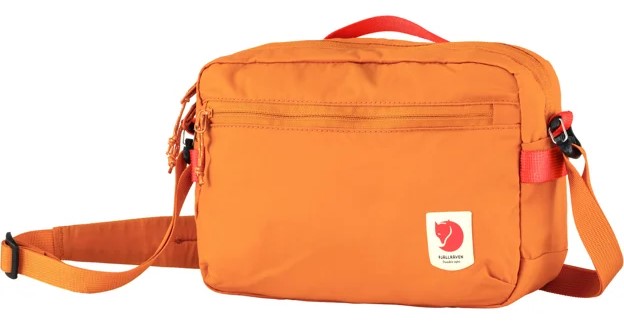 Orange fabric camera bag with red handle and shoulder strap, a front zipper compartment and a small rectangular logo with a red fox.
