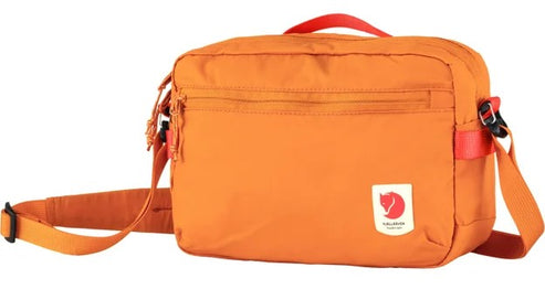 Orange fabric camera bag with red handle and shoulder strap, a front zipper compartment and a small rectangular logo with a red fox.