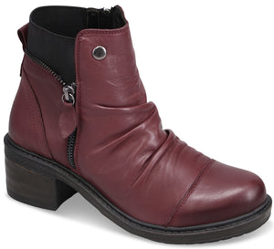 A maroon ankle boot with a rounded toe, a ruched upper, a side zipper with a small pull tab, a decorative metal button near the top, and a stacked block heel.