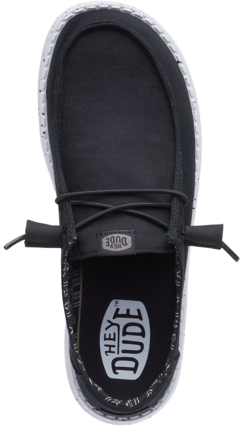 Top-down view of a black slip-on shoe with a white sole and black laces.