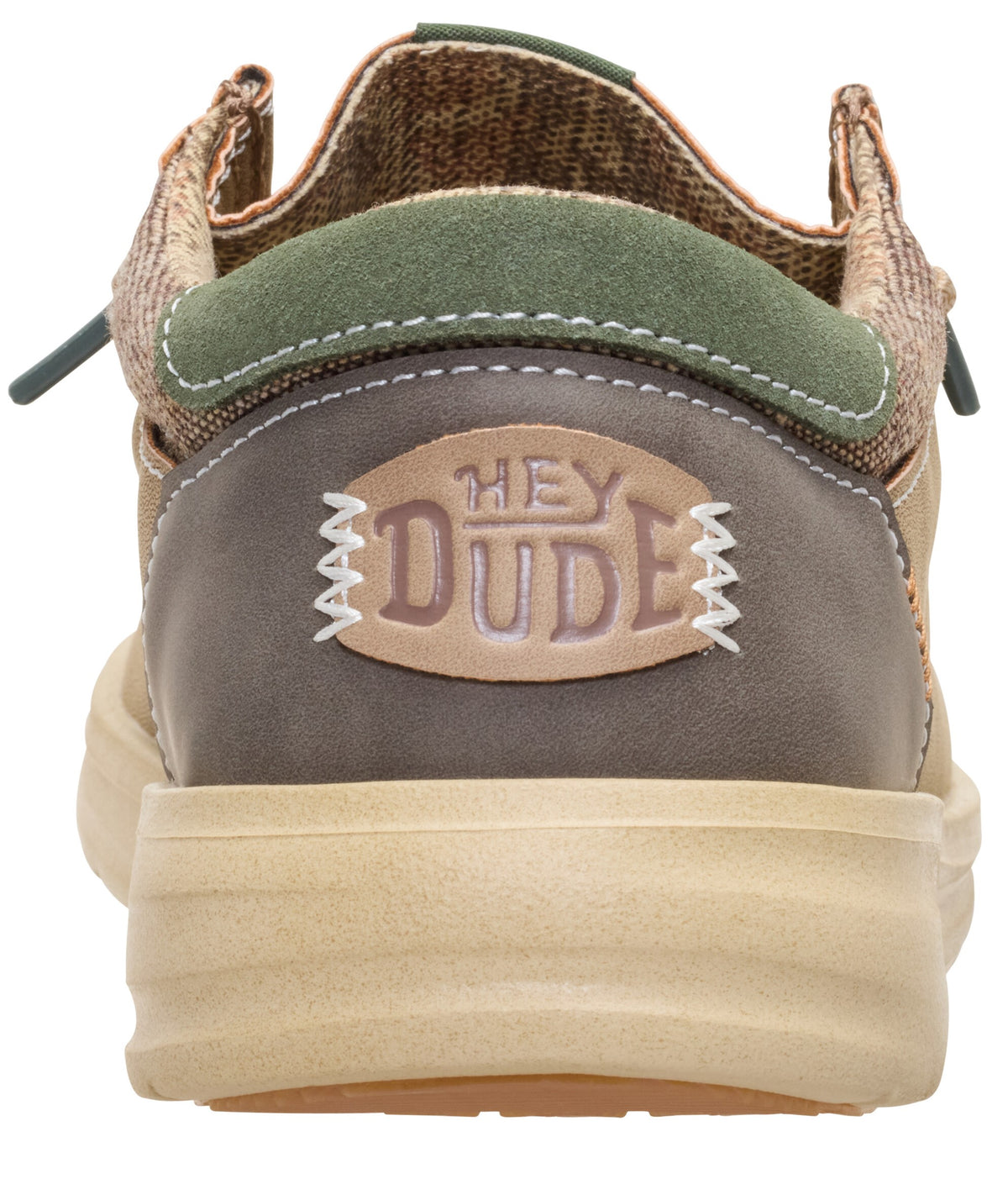 A rear-view close-up of a tan, olive green, and brown casual slip-on shoe with a tan platform sole and a patch on the heel that reads HEY DUDE in a stylized font.