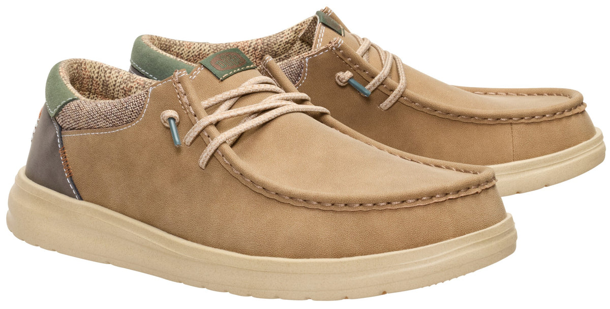 A pair of tan, slip-on casual shoes with a moc-toe design, light beige laces, a textured light brown collar with a green accent on the heel, and a thick, matching tan rubber sole.