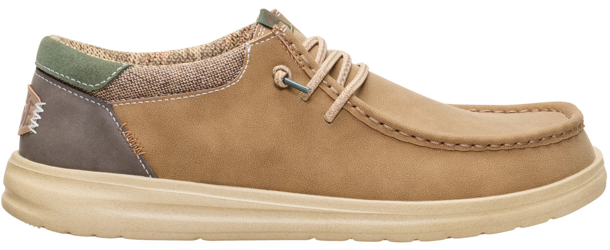 A tan slip-on shoe with a moccasin-style toe, a brown suede-like heel counter with a small woven label, a green accent at the collar, textured textile paneling, and a thick, light-tan rubber sole with light-colored laces.