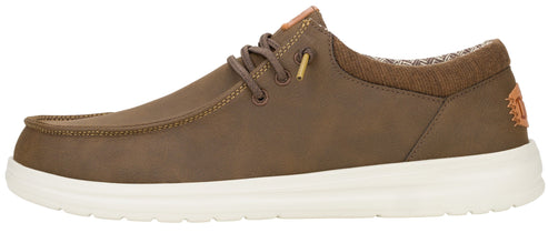 A side profile of a brown, moccasin-style sneaker with a thick white rubber sole, tan laces, and a small tan patch on the heel.