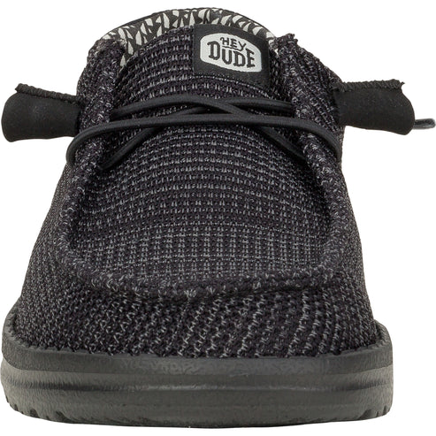 Black slip-on shoe with faux laces and a label that reads, "HEY DUDE".
