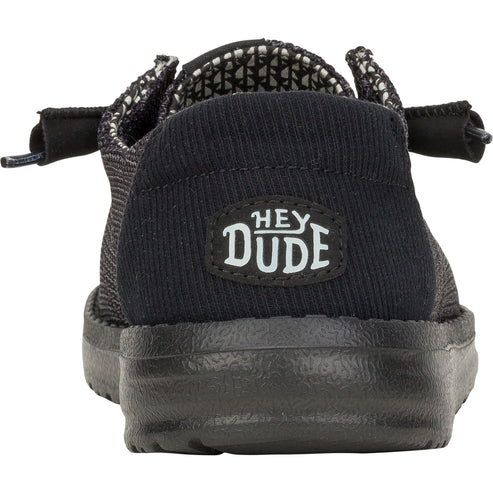 Back view of a black loafer style shoe with a black corduroy heel patch labeled "HEY DUDE".