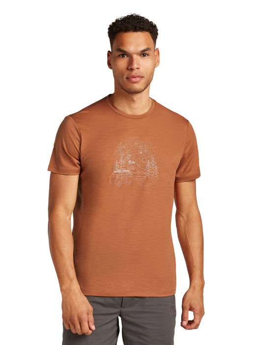 A slim man wears a brown t-shirt with a stylized white mountain graphic.