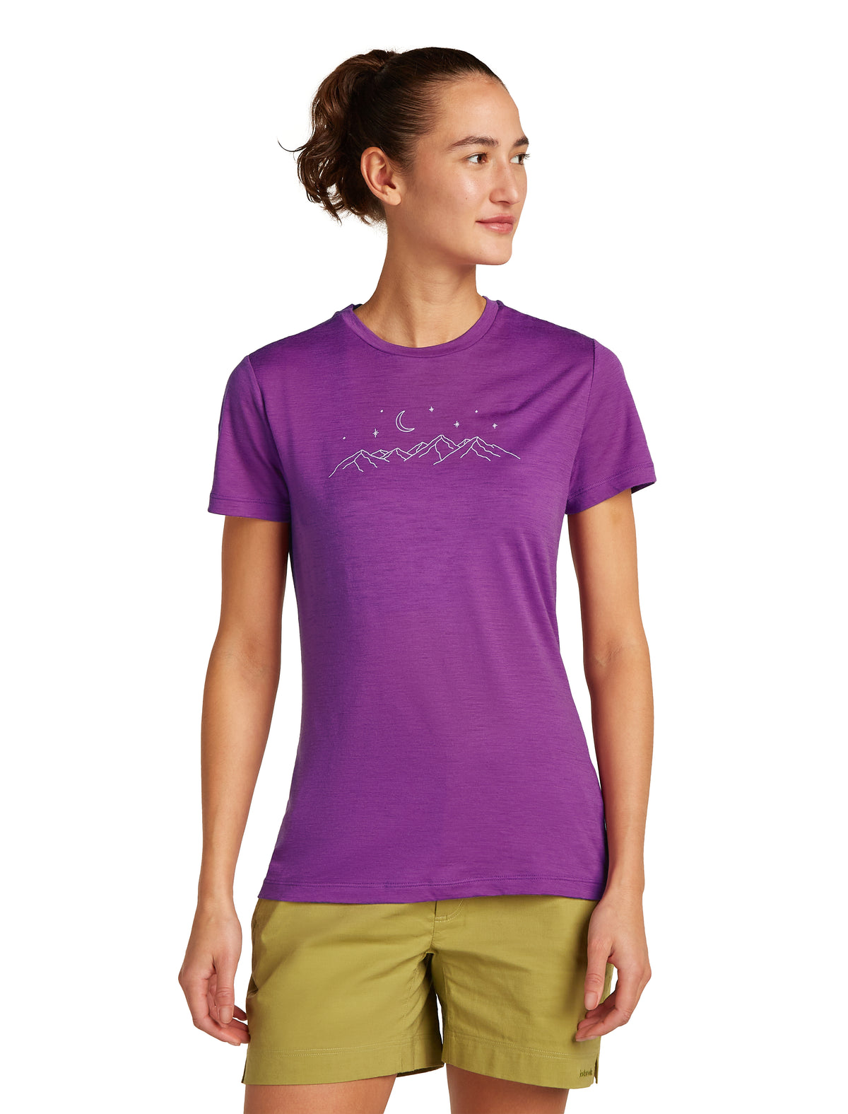 A woman wearing a purple T-shirt with a mountain line drawing and green shorts is standing.