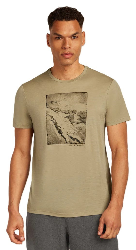 A person wearing a short-sleeved, olive green t-shirt with a rectangular graphic of a mountain range on the front.