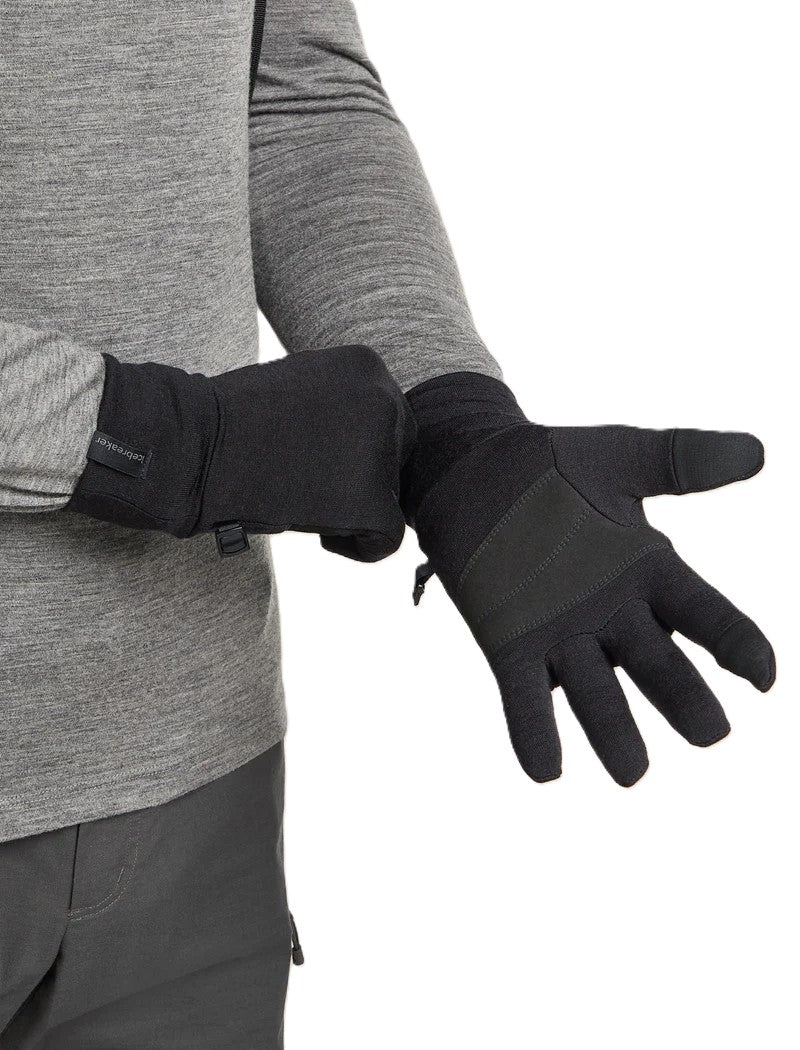 A person wearing black gloves with a gray long-sleeved shirt and gray pants is adjusting the gloves on their hands.