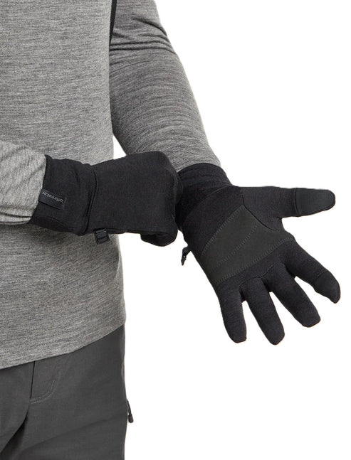 A person wearing black gloves with a gray long-sleeved shirt and gray pants is adjusting the gloves on their hands.