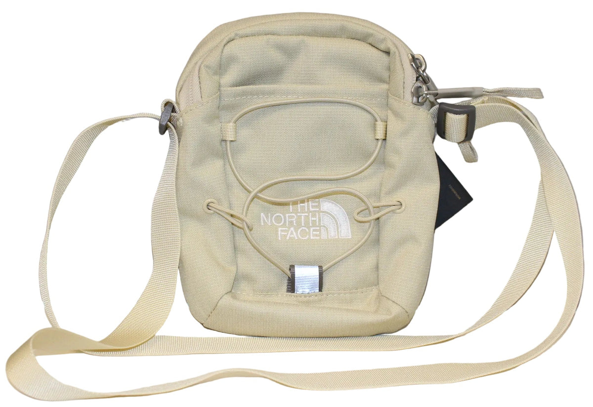 A beige crossbody bag featuring an adjustable strap, a zippered top, and a bungee cord system on the front with The North Face logo printed in white.