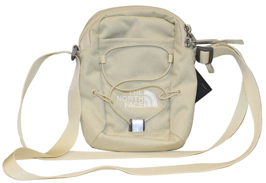A beige crossbody bag featuring an adjustable strap, a zippered top, and a bungee cord system on the front with The North Face logo printed in white.