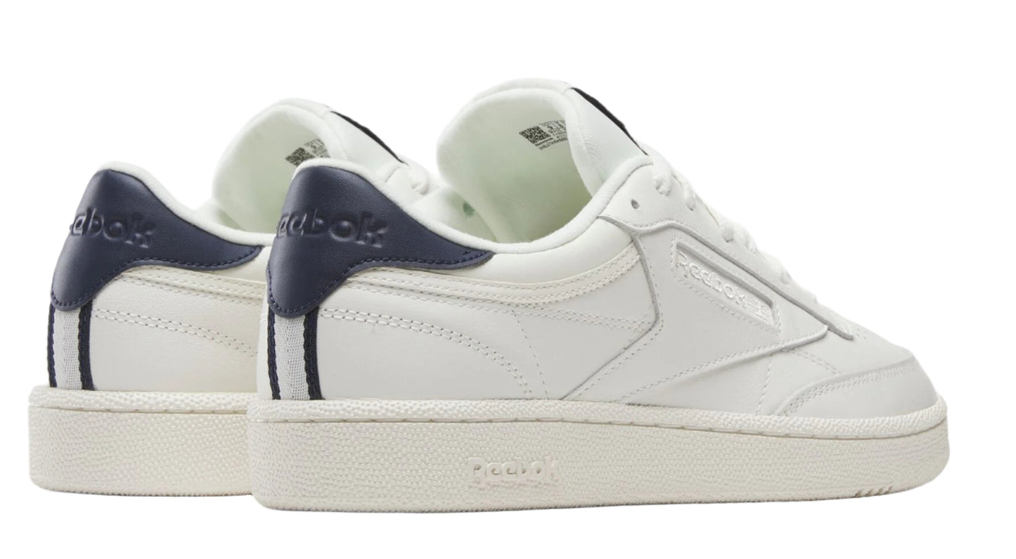 Low-top sneakers with white leather uppers, navy heel tabs with white text, and off-white rubber soles.