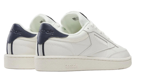 Low-top sneakers with white leather uppers, navy heel tabs with white text, and off-white rubber soles.