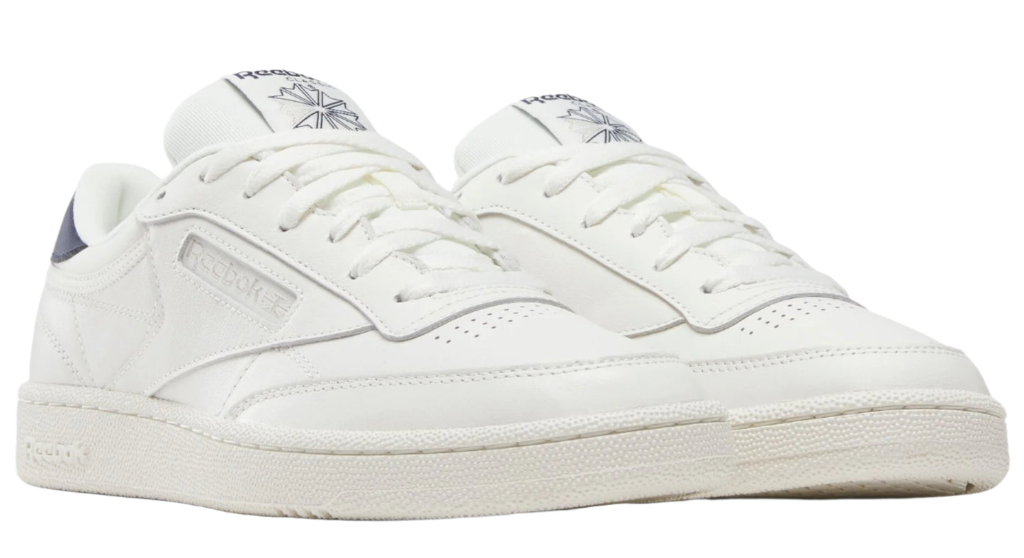 Pair of low-cut, all-white sneakers with navy blue accent on the heel.