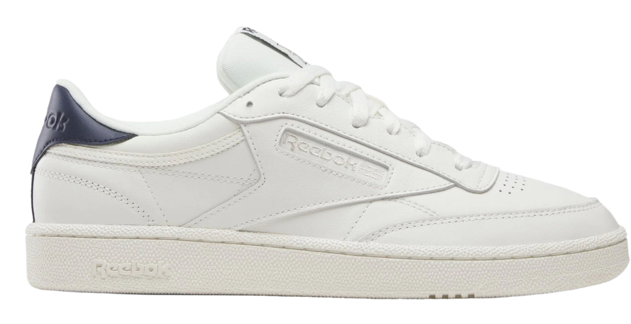 A white low-top sneaker with a navy blue heel.