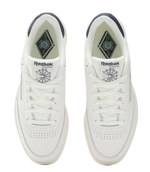 Pair of white low-top sneakers with lace-up closure, visible logo on tongue and sides, and perforated toe box.