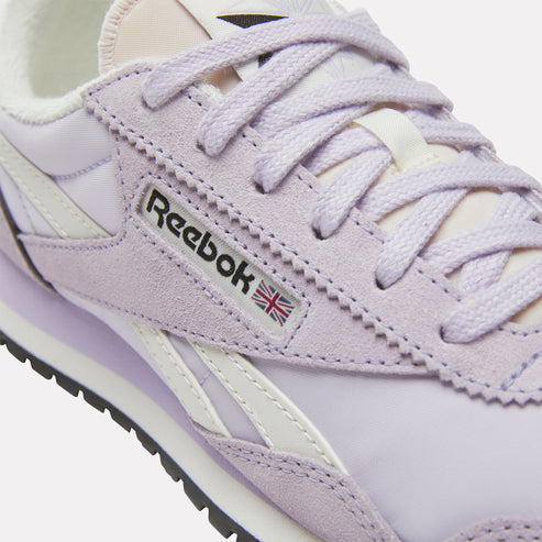 Close-up of a lavender sneaker with white accents, featuring the Reebok logo next to a British flag.