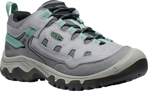 A gray hiking shoe with light blue accents, featuring a multi-textured mesh and suede upper, black laces, a reinforced toe cap, and a rugged, thick rubber sole with a Keen logo on the side.