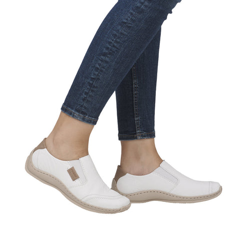 White slip-on shoes with tan soles and accents on a person wearing jeans.
