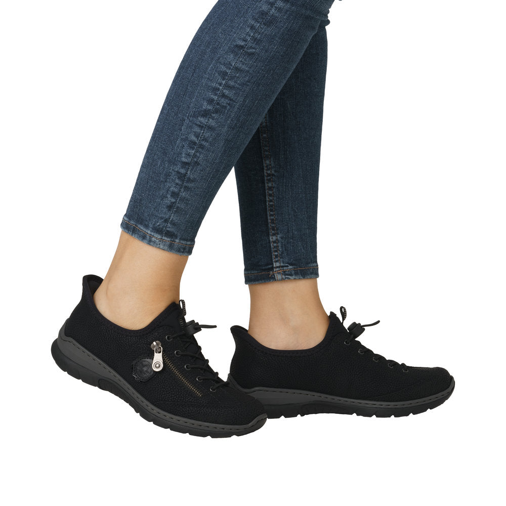 Person wearing blue jeans and black sneakers with laces and a zipper.