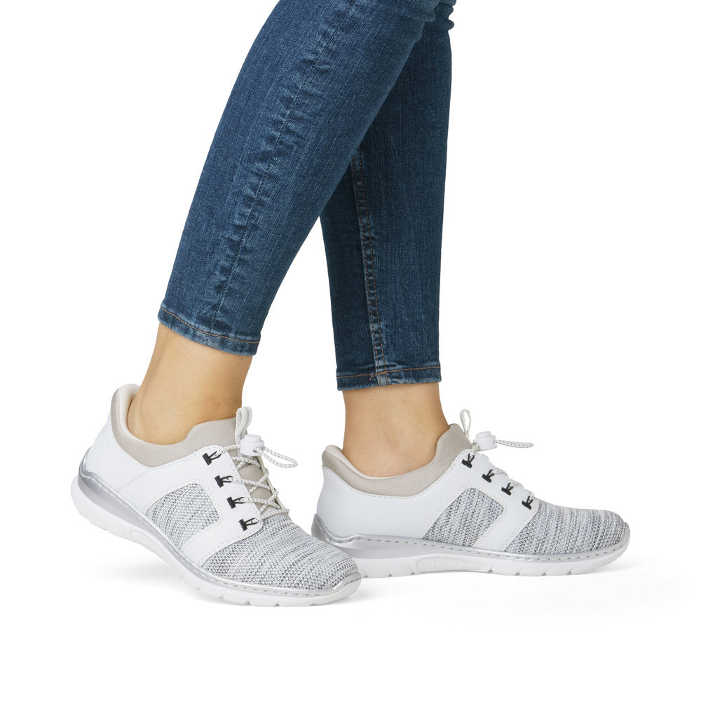 A pair of women's athletic shoes with white laces, a grey and white striped fabric across the top, and a white sole, being worn with blue jeans.