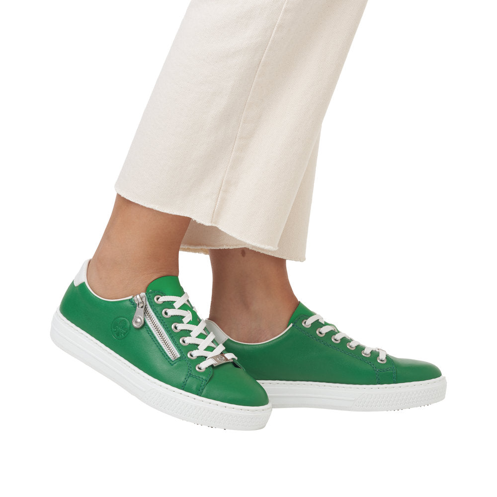 A person wearing green leather sneakers with a white sole and laces and a side zipper.