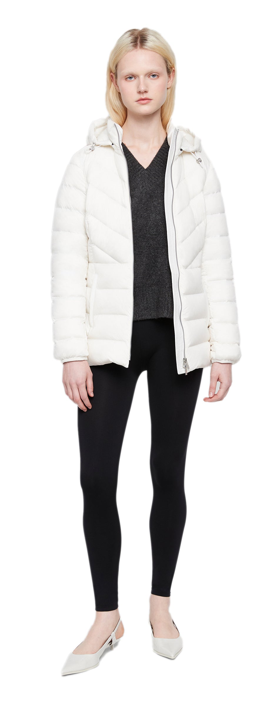 A person wearing a black top and leggings under a white quilted coat with a hood.