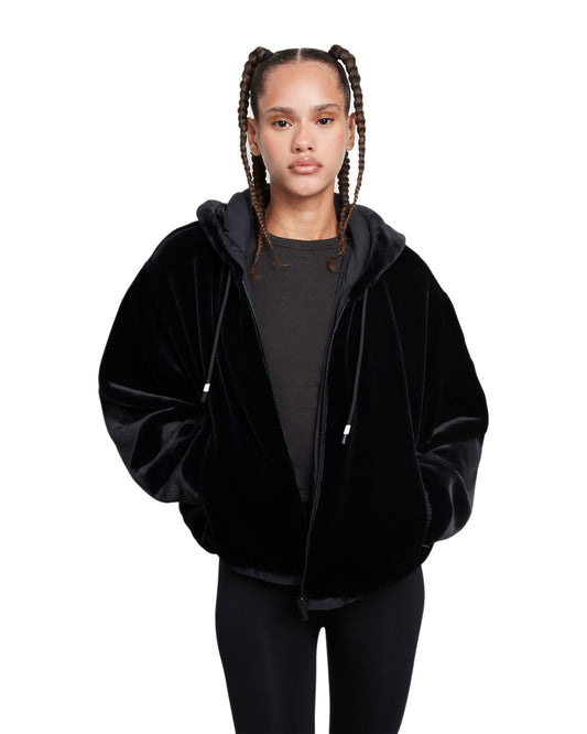 A woman with braided hair wears a black, faux fur hoodie and leggings.