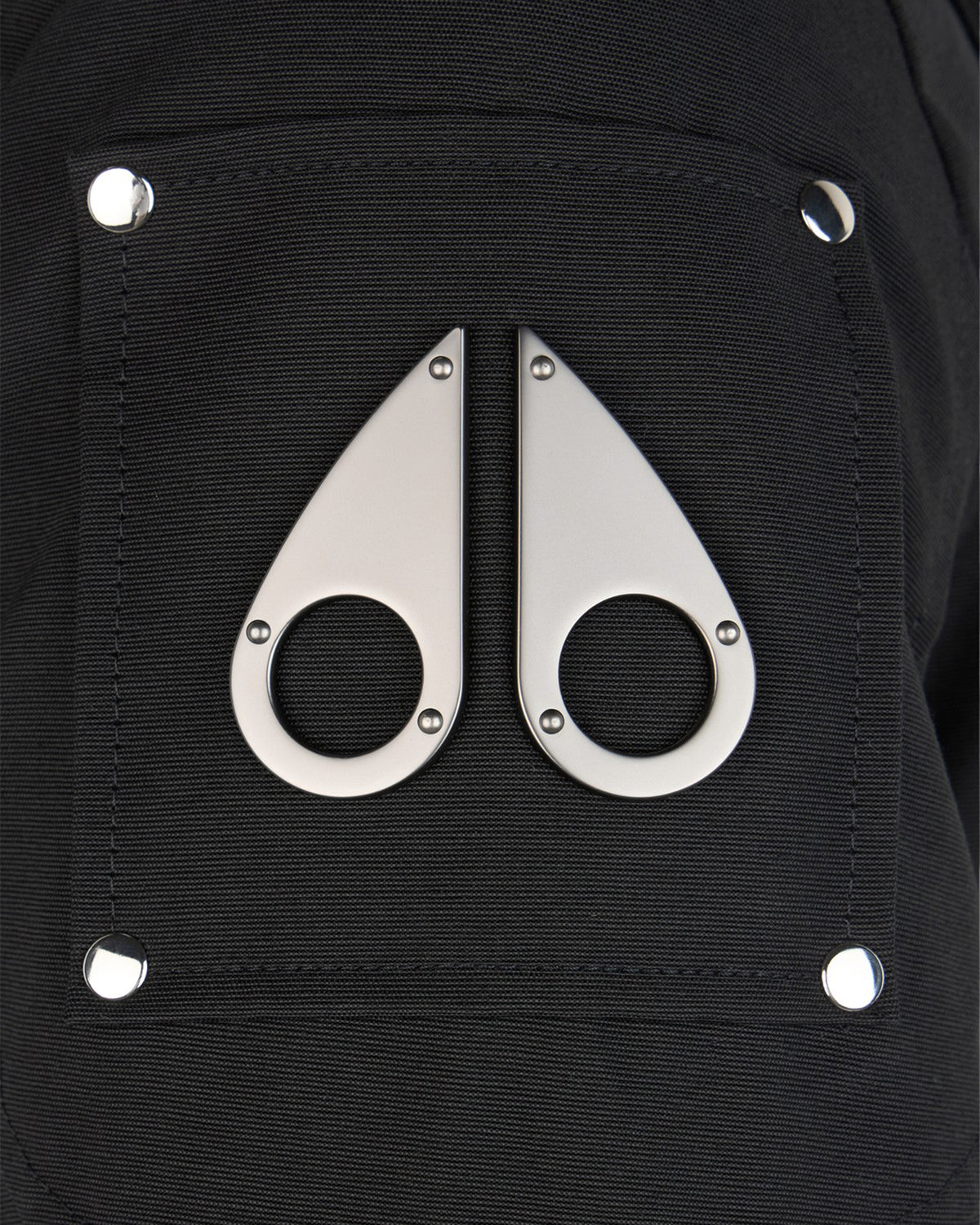 Close-up of black fabric pocket with metal accents; two teardrop shapes with circular holes in the center are oriented vertically.