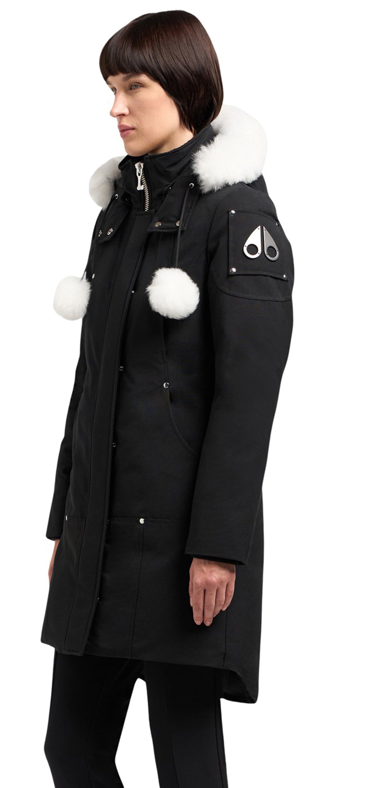 A person wearing a long black coat with white fur trim on the hood and white pom-poms on the front.