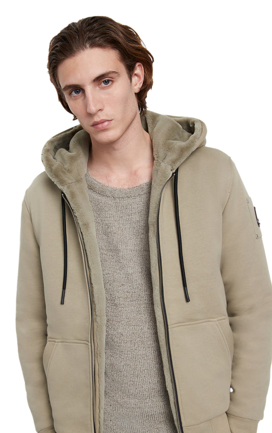 Man wearing beige zip up hoodie with fur lining and a grey sweater.