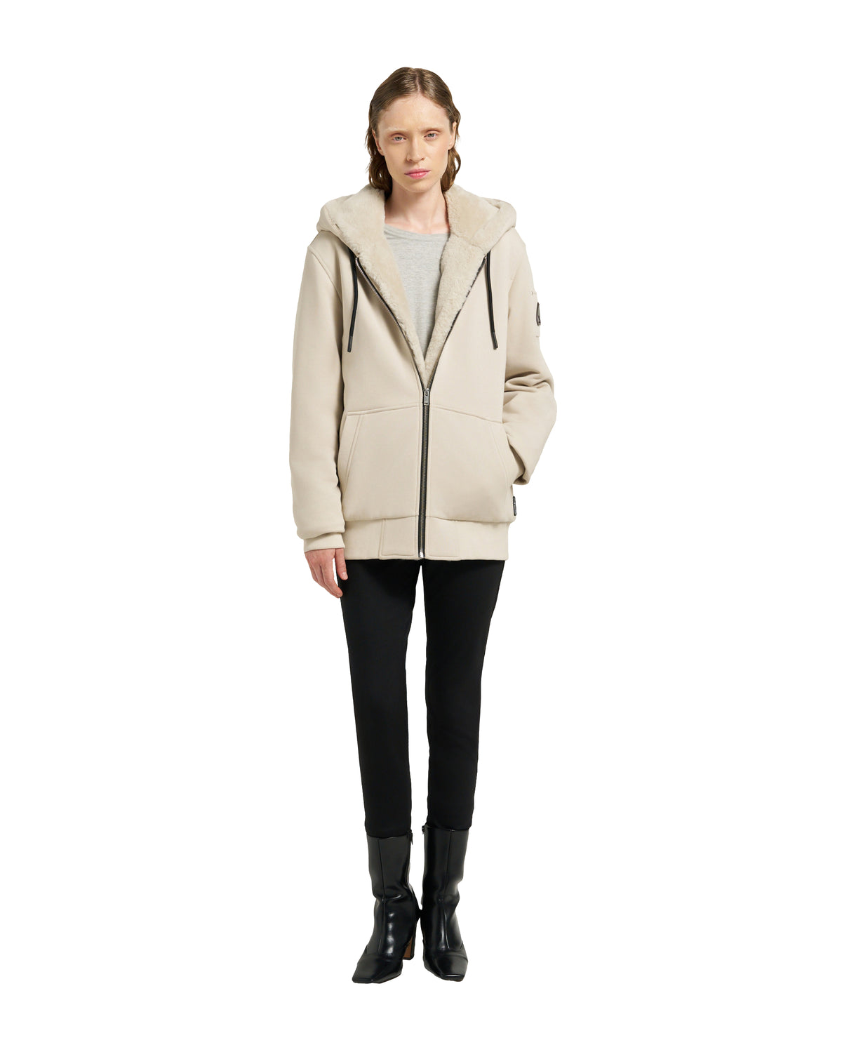 A woman in a cream, hooded jacket with black pants and boots.