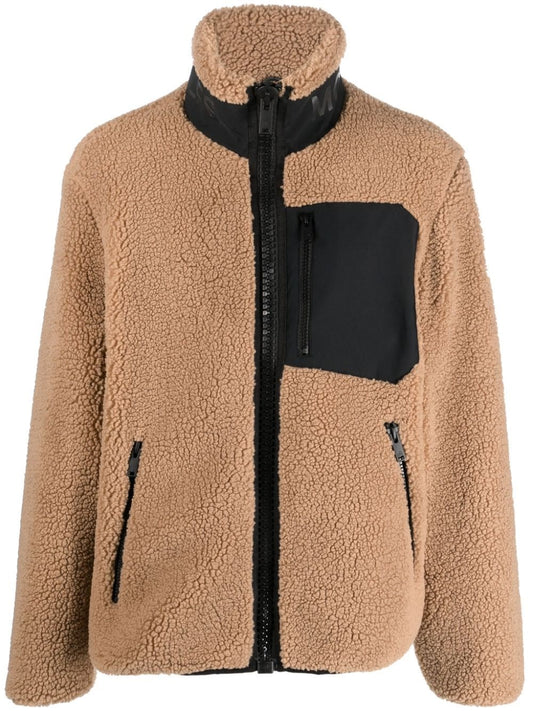 Tan, fluffy, fleece jacket with black trim on the neck, a black chest pocket, and a full black zipper.