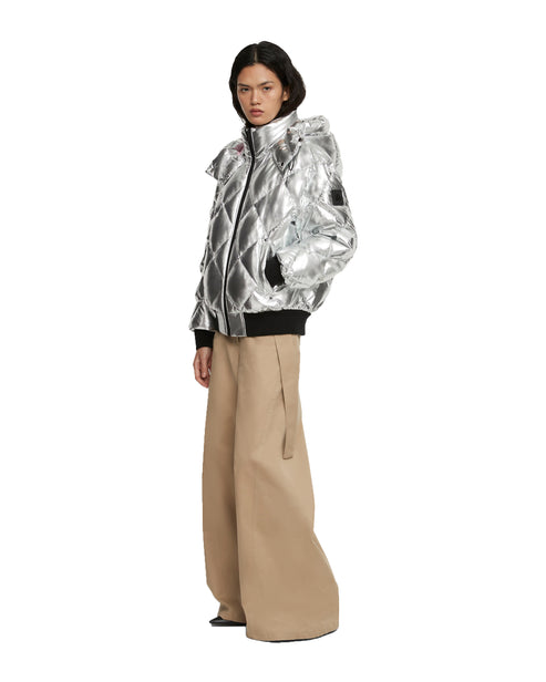 A model wearing a silver quilted hooded jacket with black wristbands and beige wide-legged pants.