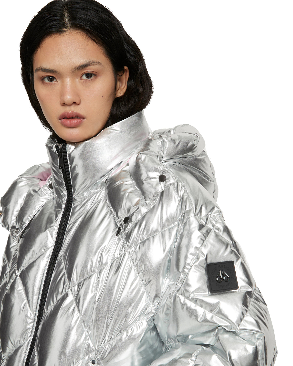 Silver puffer jacket with a black zipper and a small black patch logo on the sleeve.