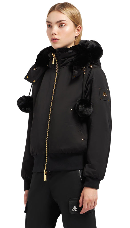 A woman in a black fur trimmed hooded jacket with pom poms and gold zippers.