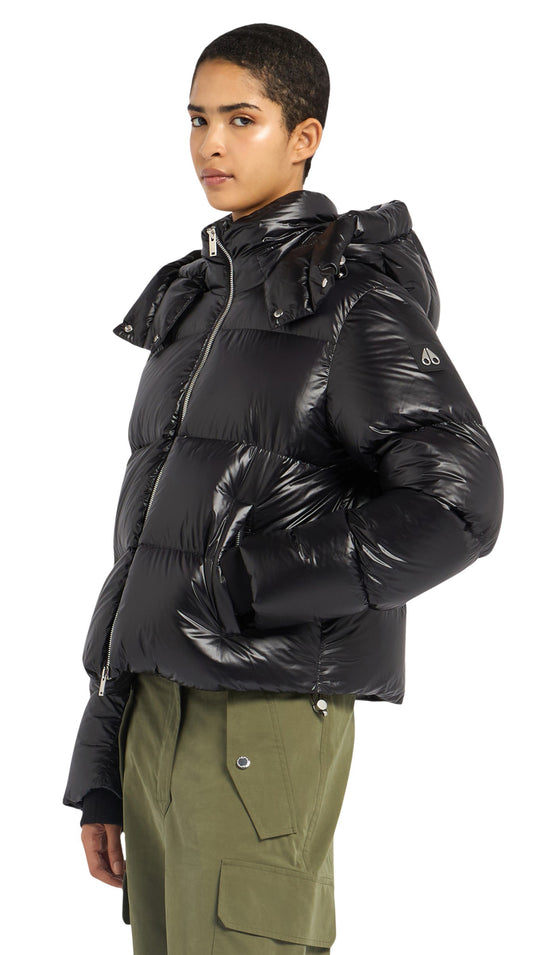 A woman in a shiny, black, hooded puffer jacket with olive green pants.