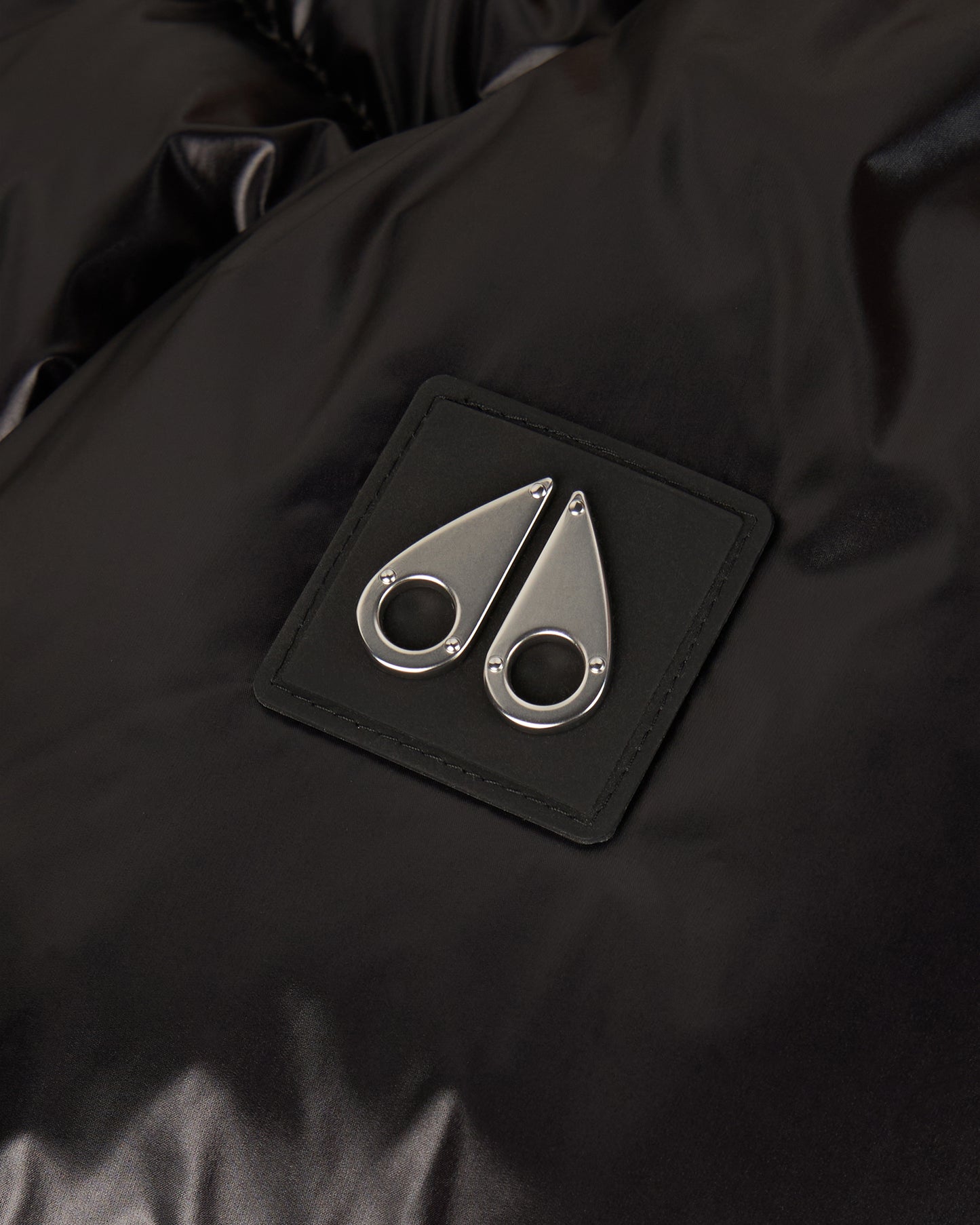Close-up of a black square patch with a silver, double teardrop logo.