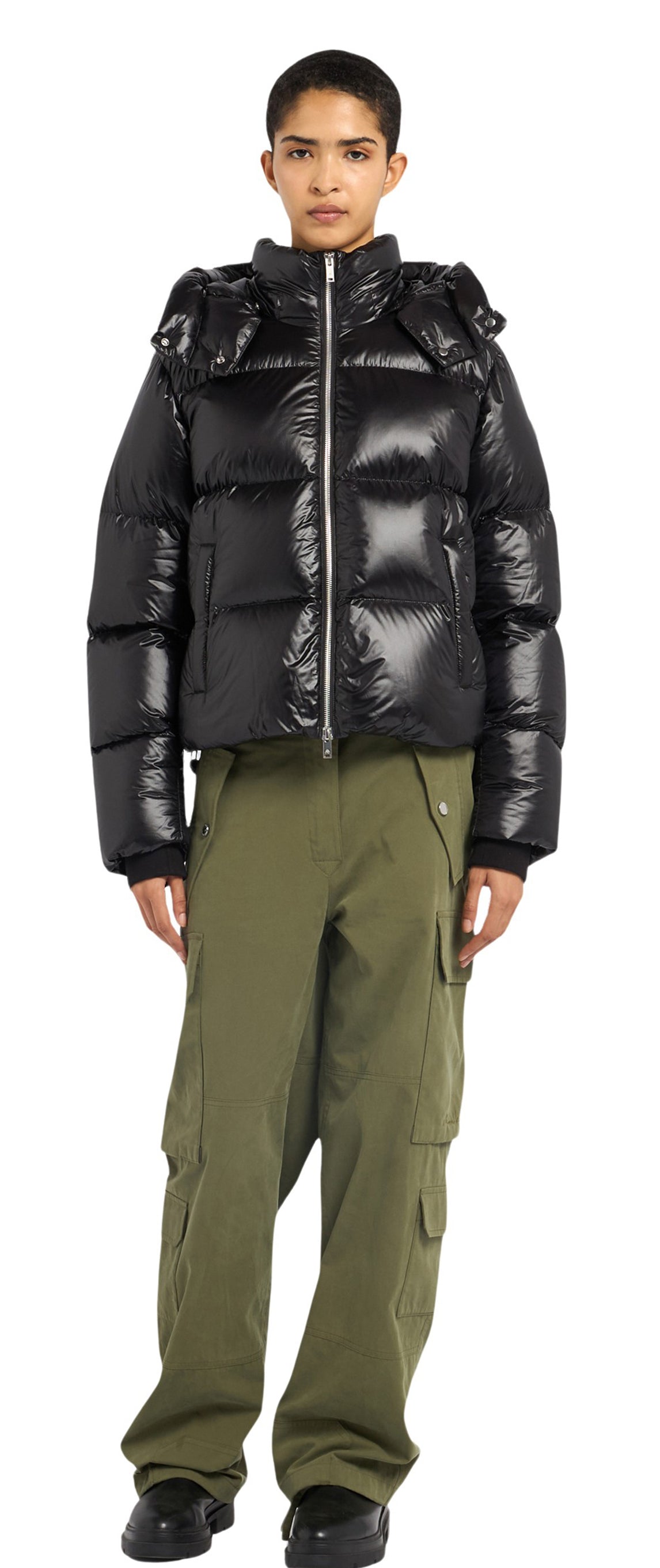 A person wearing a shiny black puffer jacket with a hood and green cargo pants.