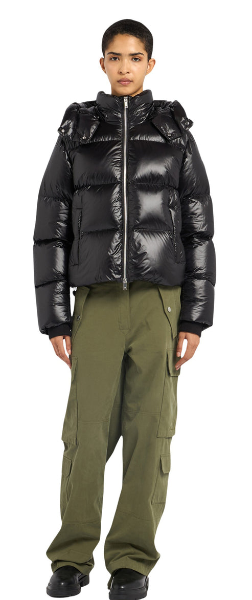 A person wearing a shiny black puffer jacket with a hood and green cargo pants.