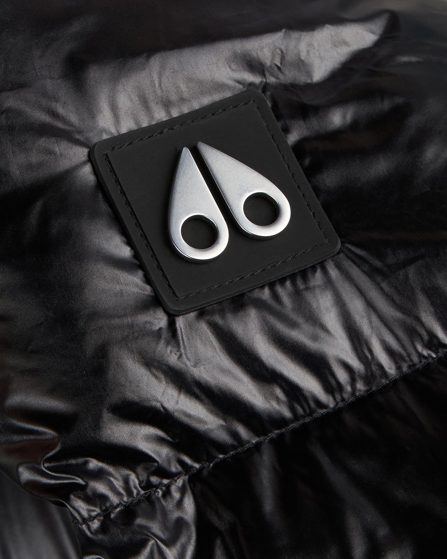Close-up of a black glossy jacket with a black square patch featuring two silver, abstract, antler-like shapes.